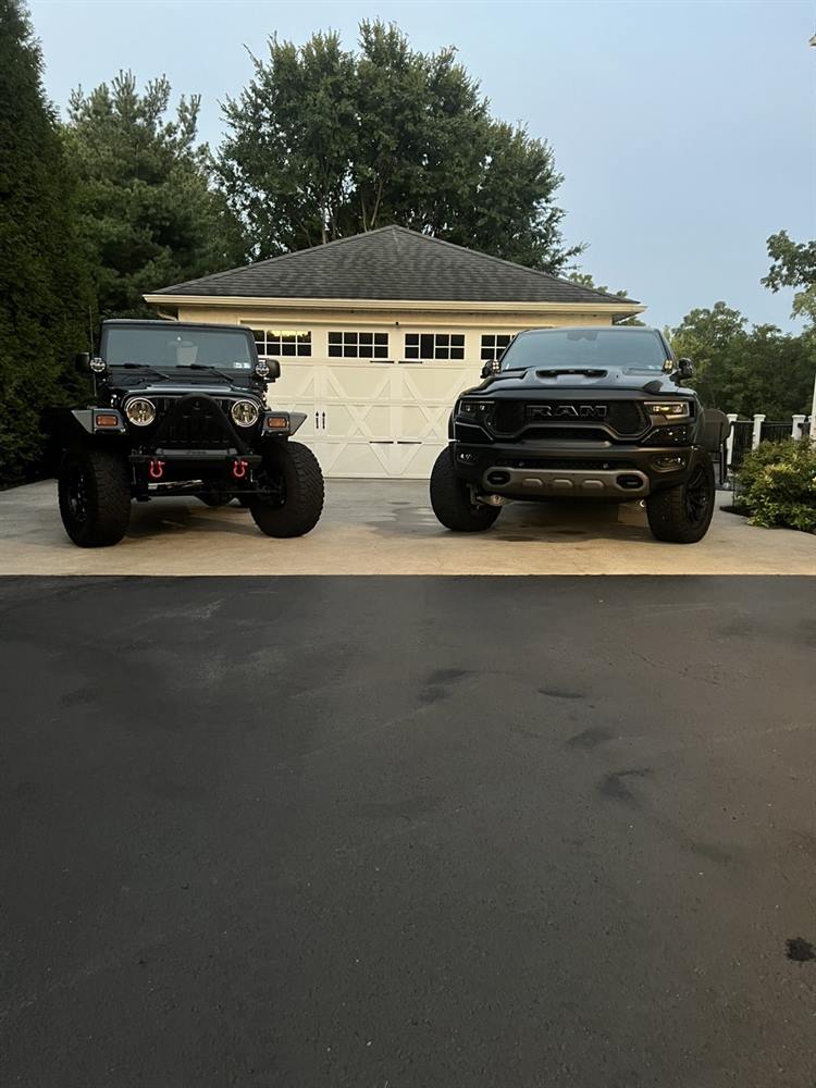 A Jeep Wrangler and Ram TRX finished side by side in front of a garage